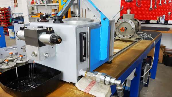 Hydraulikbehälter mit Füllstandsanzeige und angeschlossenen Leitungen auf einer Werkbank